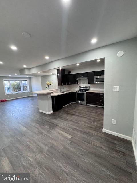 kitchen with sink, kitchen peninsula, stainless steel appliances, a breakfast bar, and dark hardwood / wood-style floors