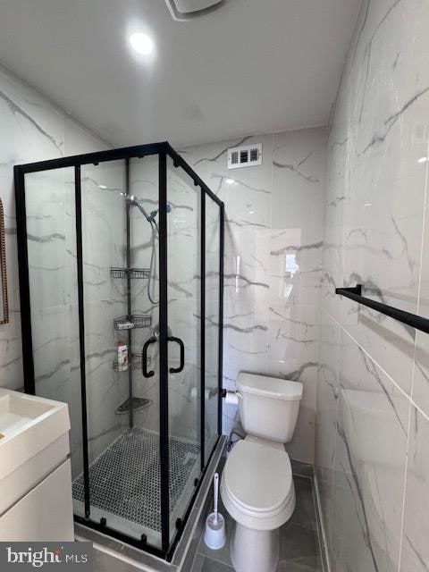 bathroom with vanity, toilet, tile walls, and a shower with door