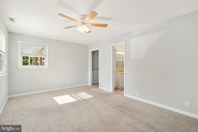 unfurnished bedroom with ensuite bathroom, radiator heating unit, light colored carpet, and ceiling fan