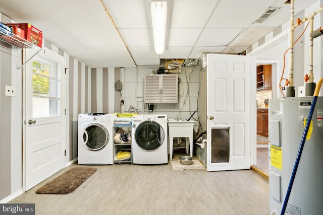 clothes washing area with electric water heater, washer and clothes dryer, and light wood-type flooring