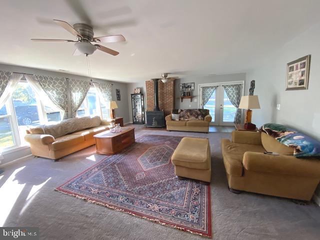 living room featuring a wood stove, a healthy amount of sunlight, carpet flooring, and ceiling fan