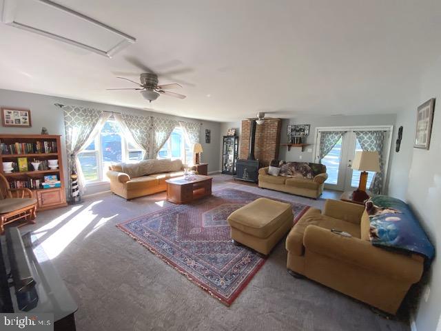 carpeted living room featuring french doors, a wood stove, and ceiling fan