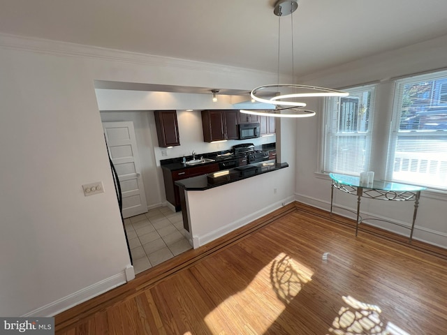 kitchen featuring stainless steel gas range, sink, dark brown cabinets, light hardwood / wood-style flooring, and pendant lighting