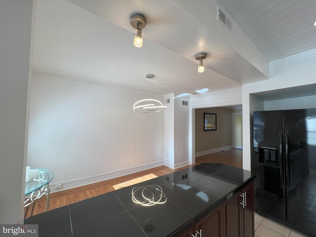 kitchen with black refrigerator with ice dispenser, pendant lighting, dark brown cabinets, and light hardwood / wood-style floors