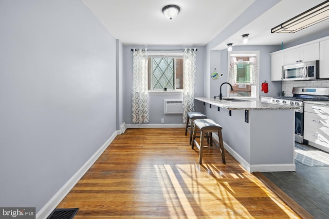 kitchen featuring a breakfast bar area, appliances with stainless steel finishes, hardwood / wood-style flooring, and white cabinetry