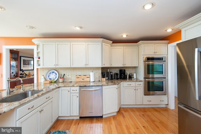 kitchen featuring light stone counters, sink, light hardwood / wood-style flooring, stainless steel appliances, and decorative backsplash