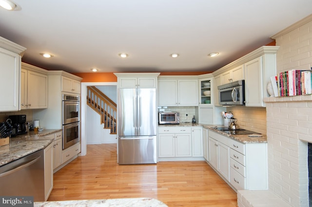 kitchen featuring appliances with stainless steel finishes, light wood-type flooring, light stone counters, and tasteful backsplash