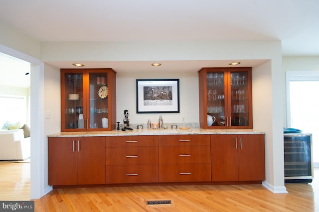 bar with a wealth of natural light, light stone counters, and light wood-type flooring