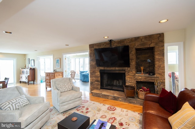 living room with a wealth of natural light, a stone fireplace, and wood-type flooring