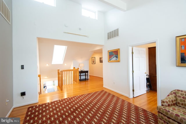 living room with wood-type flooring, high vaulted ceiling, a skylight, and beamed ceiling