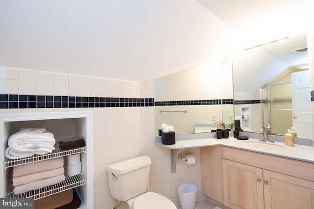 bathroom with toilet, vaulted ceiling, tile walls, a shower with door, and vanity