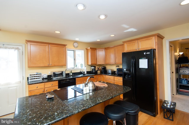 kitchen featuring a kitchen island, black appliances, dark stone countertops, light wood-type flooring, and a kitchen bar