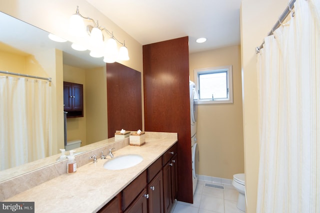 bathroom featuring stacked washer and clothes dryer, tile patterned floors, vanity, and toilet