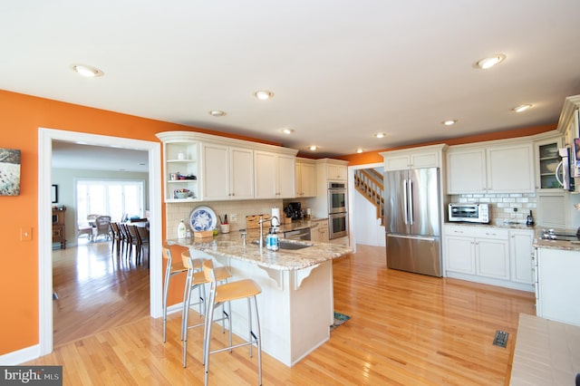 kitchen with light wood-type flooring, tasteful backsplash, sink, kitchen peninsula, and appliances with stainless steel finishes