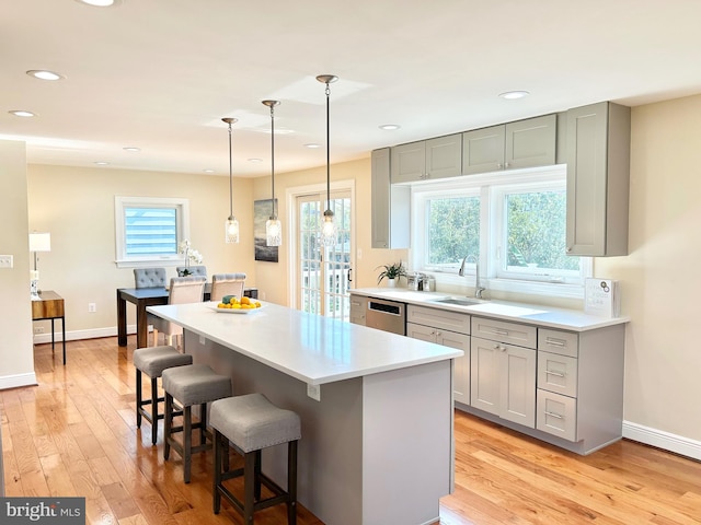 kitchen with stainless steel dishwasher, sink, light hardwood / wood-style flooring, and pendant lighting