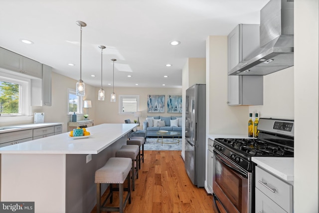 kitchen with wall chimney range hood, a kitchen breakfast bar, light hardwood / wood-style flooring, gray cabinetry, and stainless steel appliances