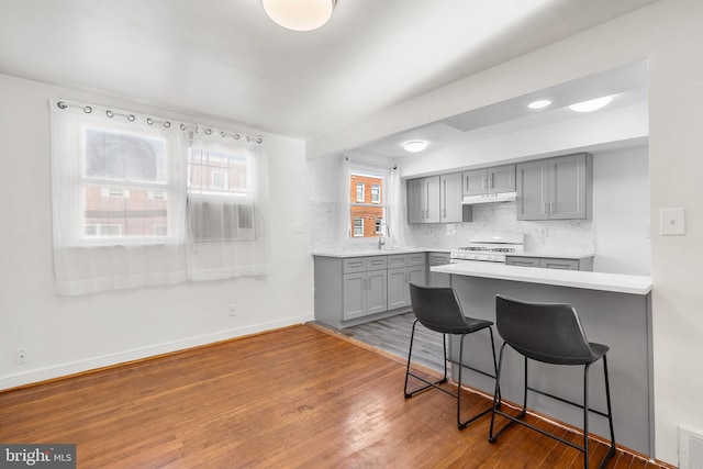 kitchen with light hardwood / wood-style flooring, white range oven, backsplash, gray cabinets, and a breakfast bar