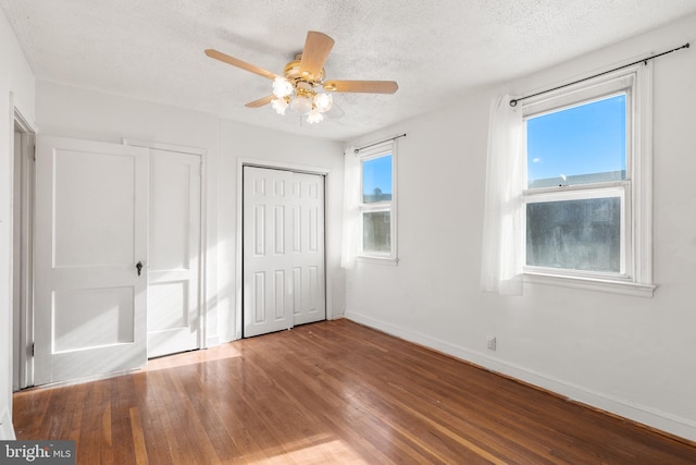 unfurnished bedroom with ceiling fan, wood-type flooring, a textured ceiling, and two closets