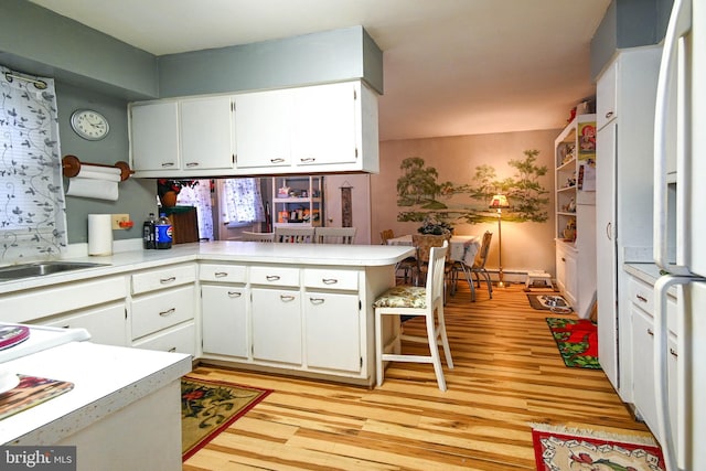 kitchen with kitchen peninsula, white cabinetry, light hardwood / wood-style flooring, and sink