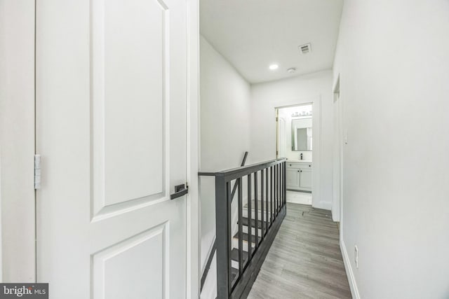 hall featuring light wood-type flooring, visible vents, baseboards, recessed lighting, and an upstairs landing