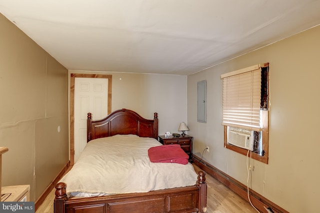 bedroom with cooling unit, electric panel, and light hardwood / wood-style floors