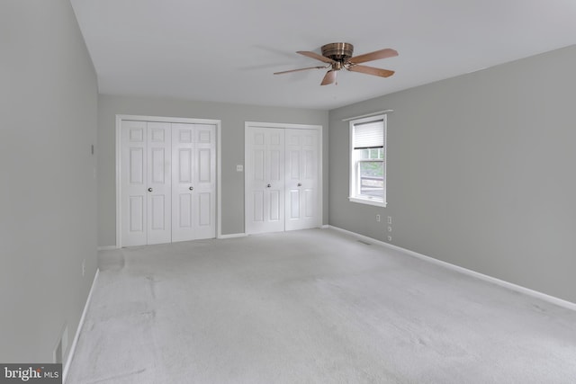 unfurnished bedroom with two closets, light colored carpet, and ceiling fan