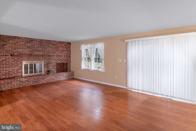 unfurnished living room featuring hardwood / wood-style flooring, a brick fireplace, and brick wall