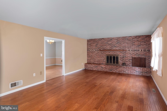 unfurnished living room with a notable chandelier, hardwood / wood-style floors, and a brick fireplace