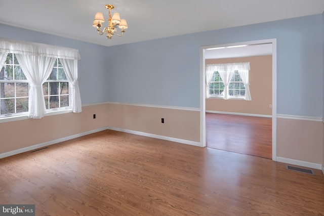 empty room with hardwood / wood-style floors and an inviting chandelier