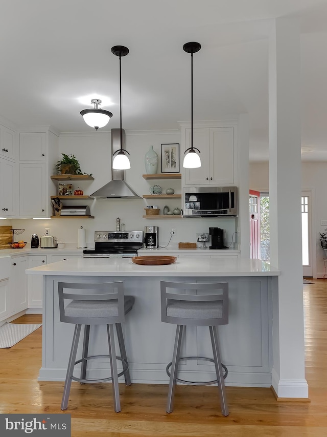 kitchen with light hardwood / wood-style flooring, white cabinets, wall chimney range hood, and appliances with stainless steel finishes