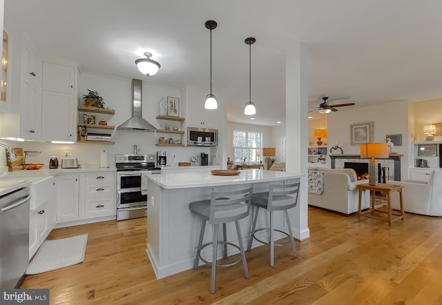 kitchen with white cabinets, light hardwood / wood-style floors, wall chimney range hood, and appliances with stainless steel finishes