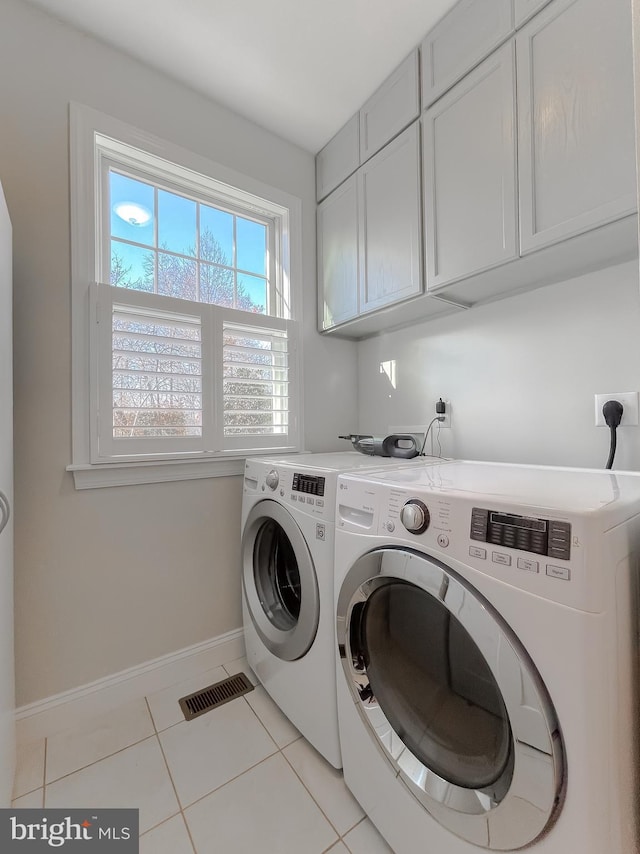 washroom featuring washing machine and clothes dryer, light tile patterned floors, and cabinets