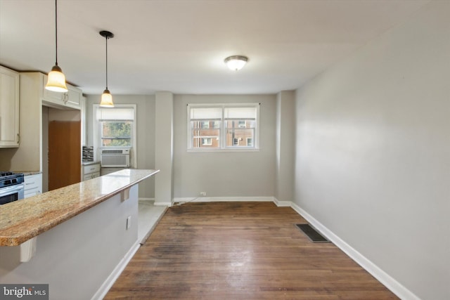 kitchen featuring cooling unit, hanging light fixtures, kitchen peninsula, dark hardwood / wood-style floors, and a kitchen bar