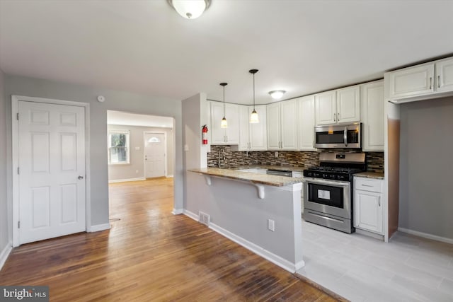 kitchen with light hardwood / wood-style floors, stainless steel appliances, kitchen peninsula, hanging light fixtures, and white cabinets