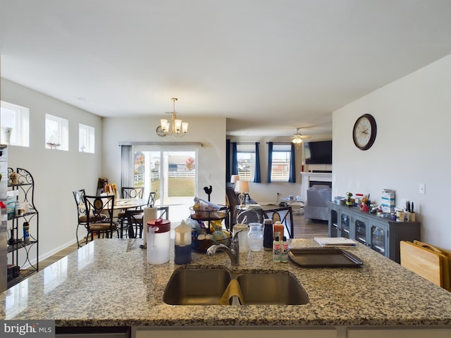 kitchen with sink, ceiling fan with notable chandelier, dark hardwood / wood-style flooring, hanging light fixtures, and light stone counters