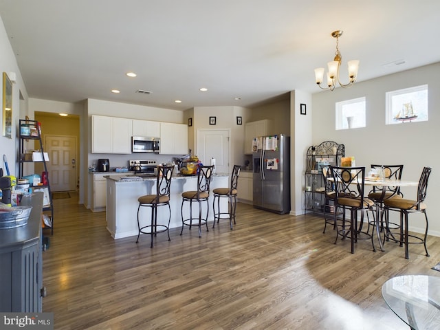 kitchen with white cabinets, appliances with stainless steel finishes, a breakfast bar, hardwood / wood-style flooring, and pendant lighting