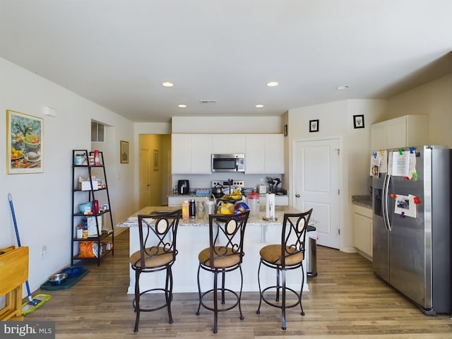 kitchen featuring white cabinets, light stone counters, a kitchen island, hardwood / wood-style flooring, and stainless steel appliances