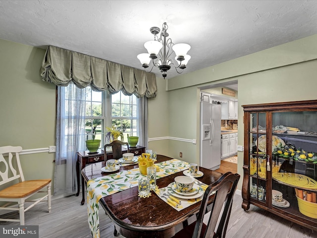 dining space with light hardwood / wood-style flooring, a textured ceiling, and a chandelier