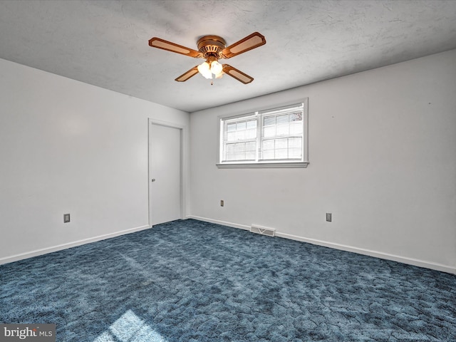 spare room featuring a textured ceiling, dark carpet, and ceiling fan