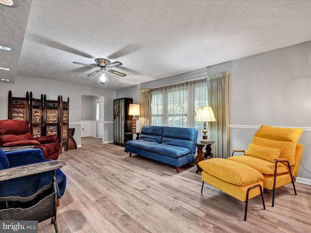 living room with light hardwood / wood-style floors, a textured ceiling, and ceiling fan