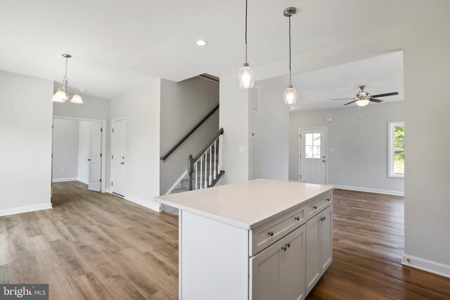 kitchen featuring white cabinets, light hardwood / wood-style flooring, ceiling fan with notable chandelier, hanging light fixtures, and a kitchen island