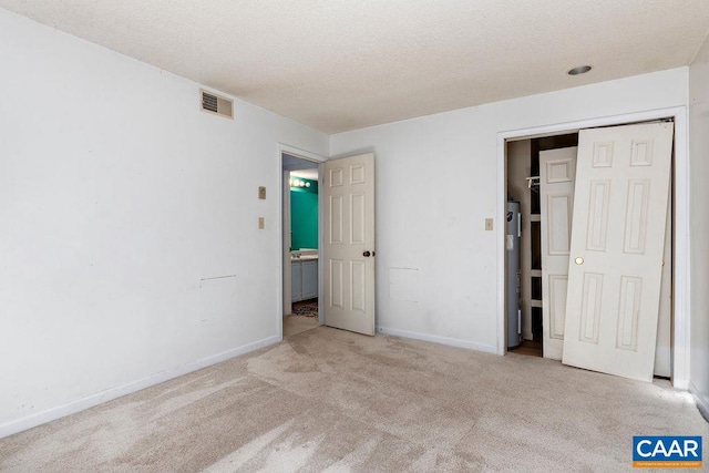 unfurnished bedroom featuring a closet, water heater, a textured ceiling, and light carpet