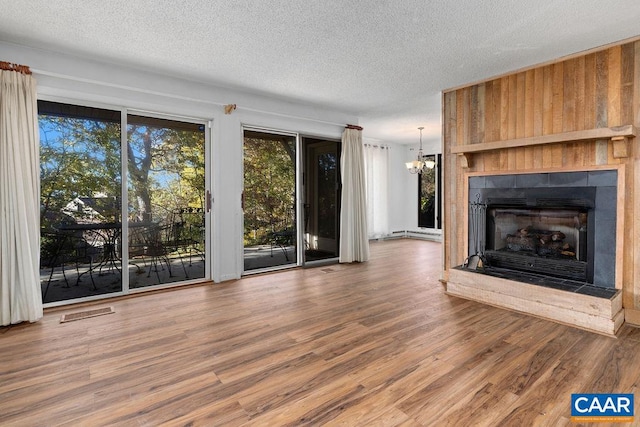 unfurnished living room with hardwood / wood-style flooring, a notable chandelier, a tiled fireplace, and a textured ceiling