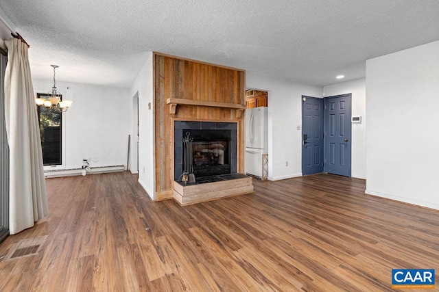 unfurnished living room with baseboard heating, dark hardwood / wood-style flooring, a tile fireplace, a chandelier, and a textured ceiling