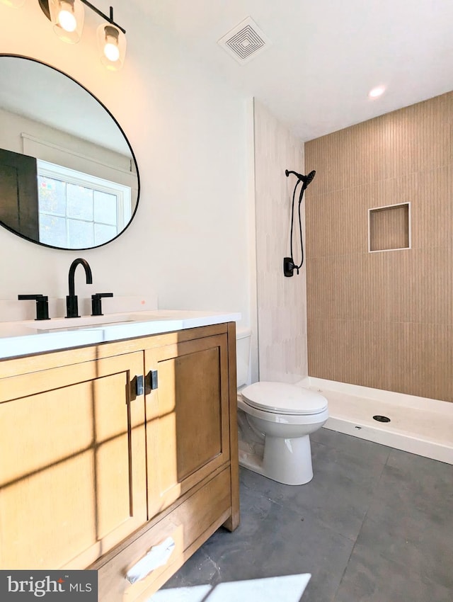 bathroom with toilet, vanity, concrete floors, and tiled shower