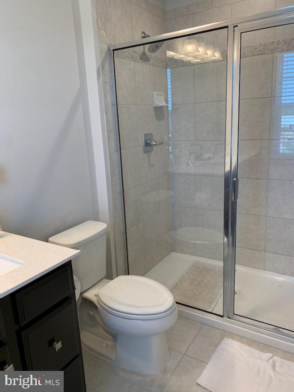 bathroom with tile patterned floors, vanity, toilet, and a shower with shower door