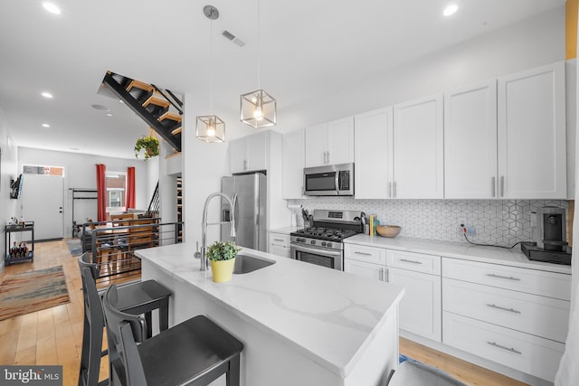 kitchen featuring light stone counters, stainless steel appliances, sink, hanging light fixtures, and light hardwood / wood-style flooring