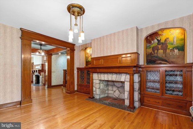 unfurnished living room featuring baseboards, light wood-style floors, a fireplace, and wallpapered walls