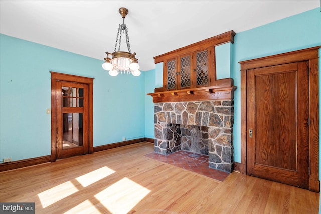 unfurnished living room with a stone fireplace, baseboards, an inviting chandelier, and wood finished floors