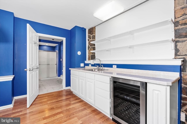 bar with indoor wet bar, baseboards, light wood-type flooring, wine cooler, and a sink